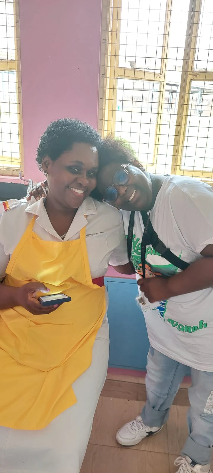 Deux femmes souriantes posent côte à côte, l’une appuyant sa tête sur l’épaule de l’autre.